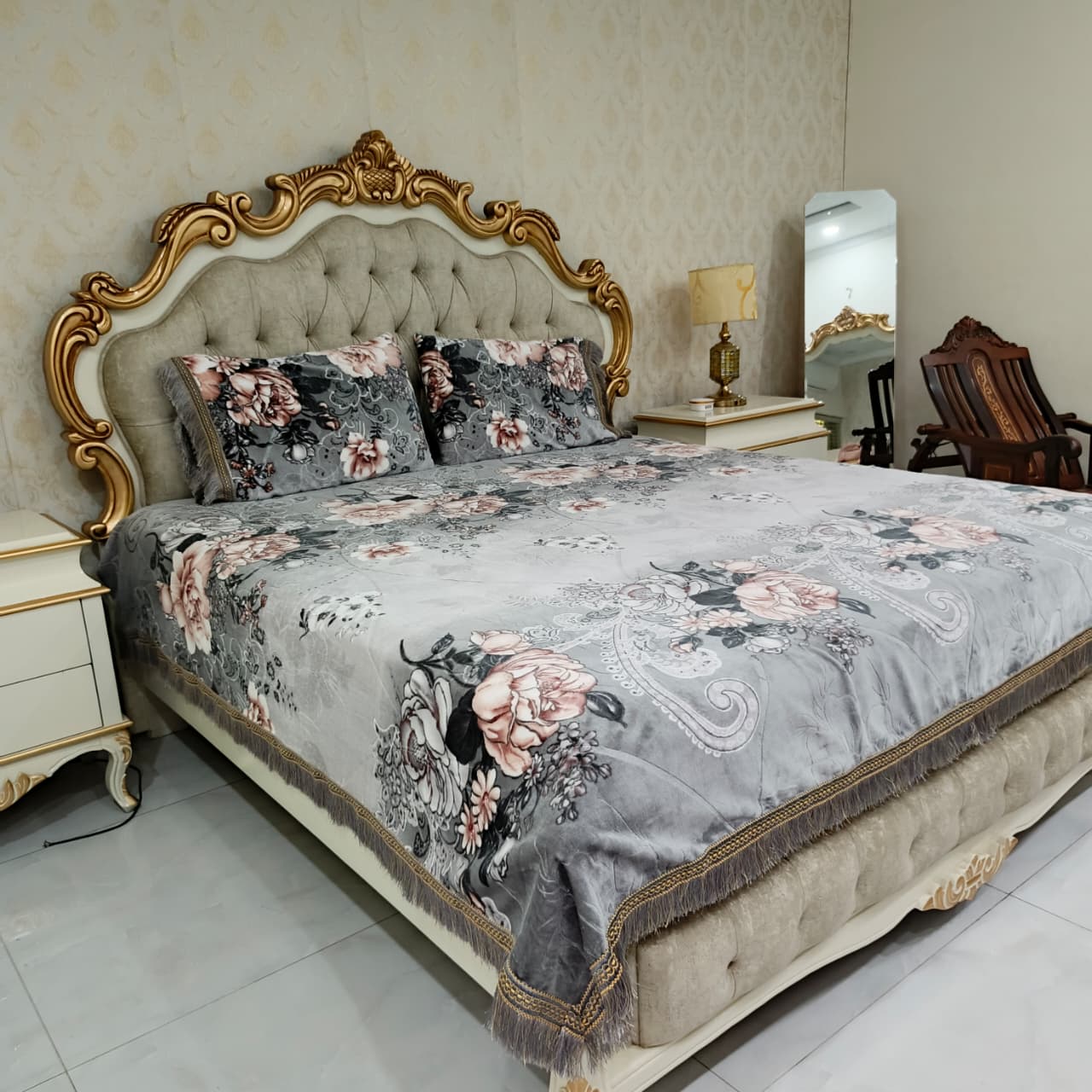 Decorative floral bedspread on a bed with ornate headboard in a bedroom setting.