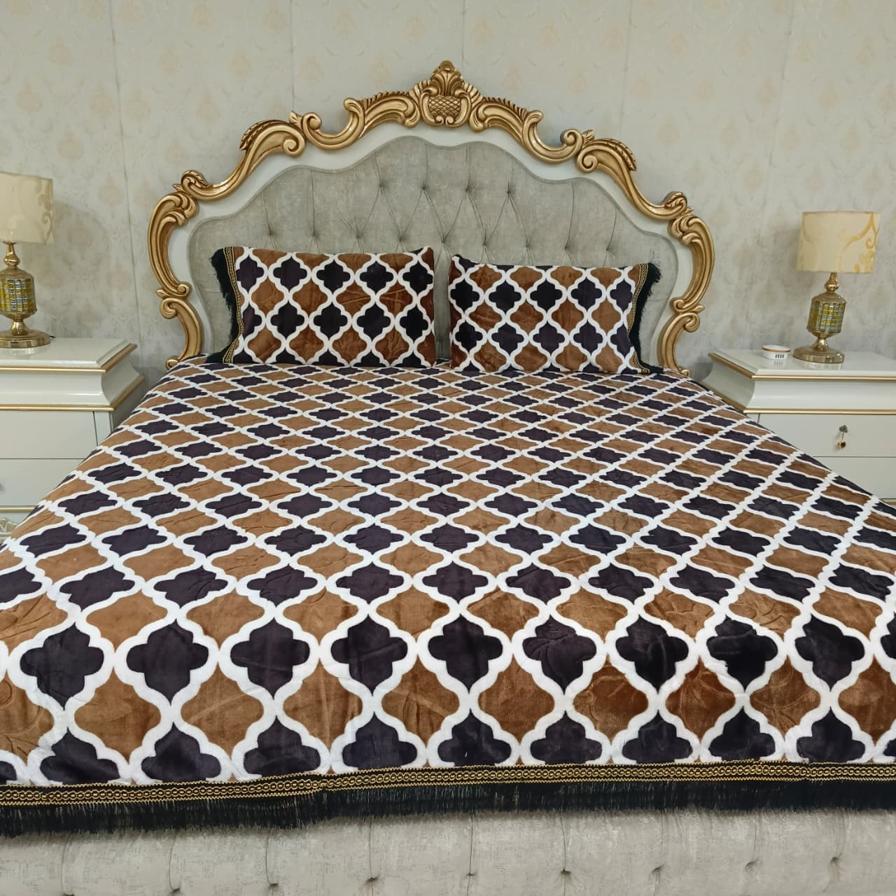 Decorative bedspread with geometric pattern on a bed with ornate headboard.