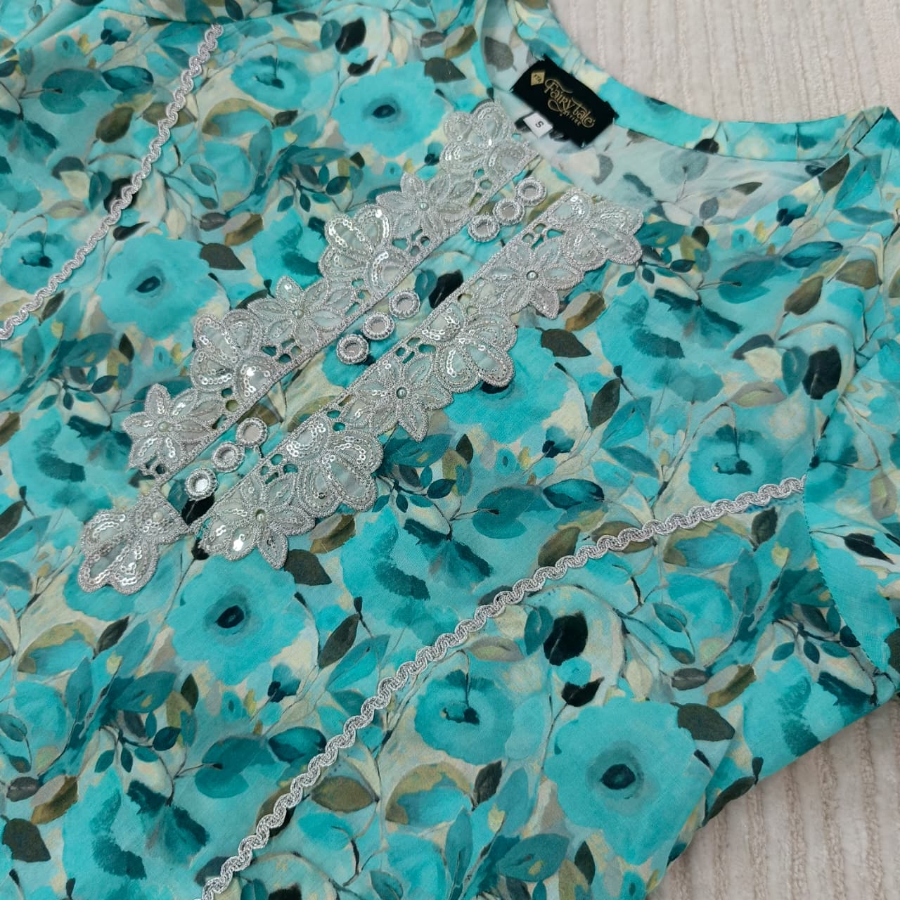 Teal floral fabric with silver lace and chain, brand label visible
Celebrate Eid with Noor-e-Zar Collection - Flat 25% Off Festive Pakistani Dresses Online
