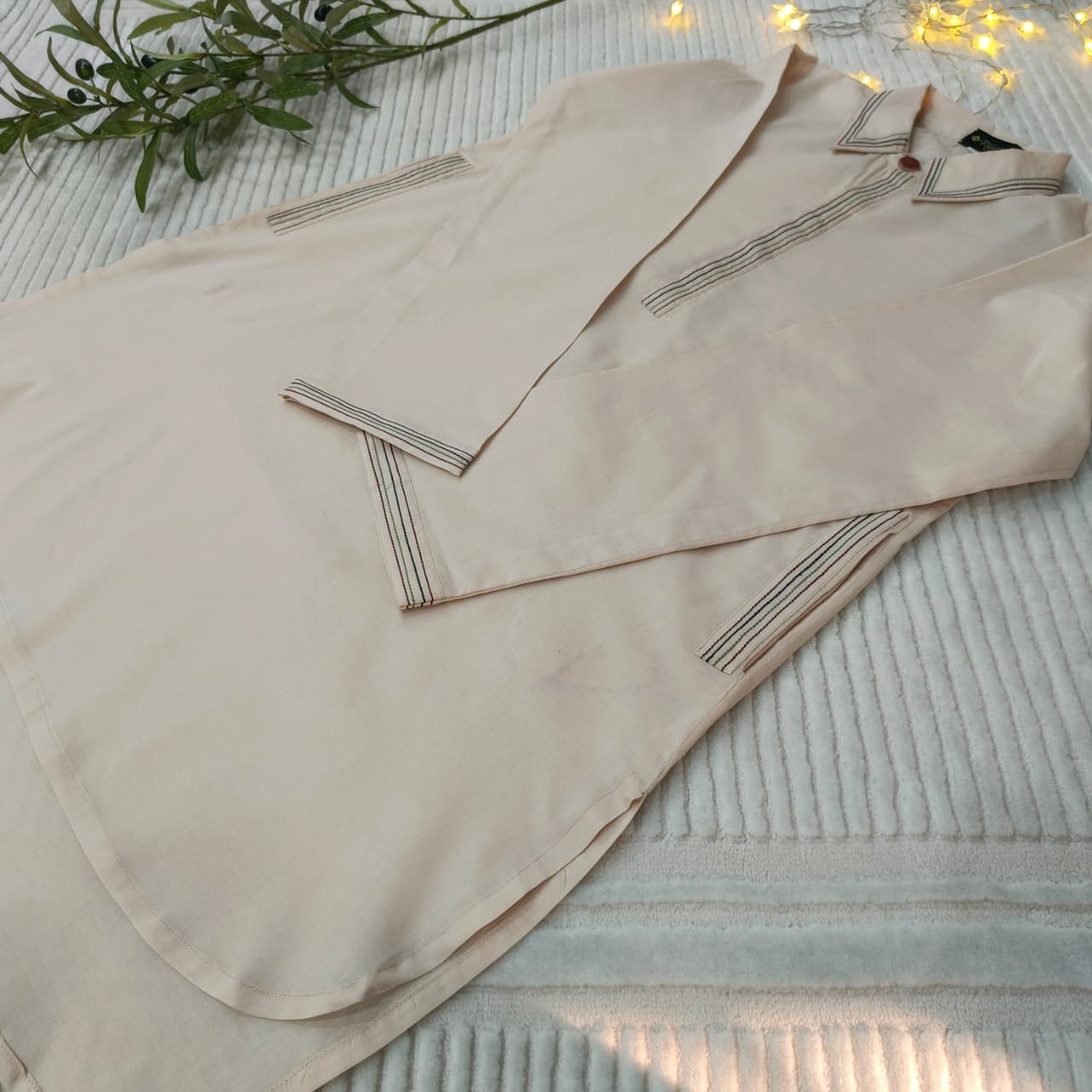 Beige shirt with embroidered details on a textured surface with greenery and lights in the background