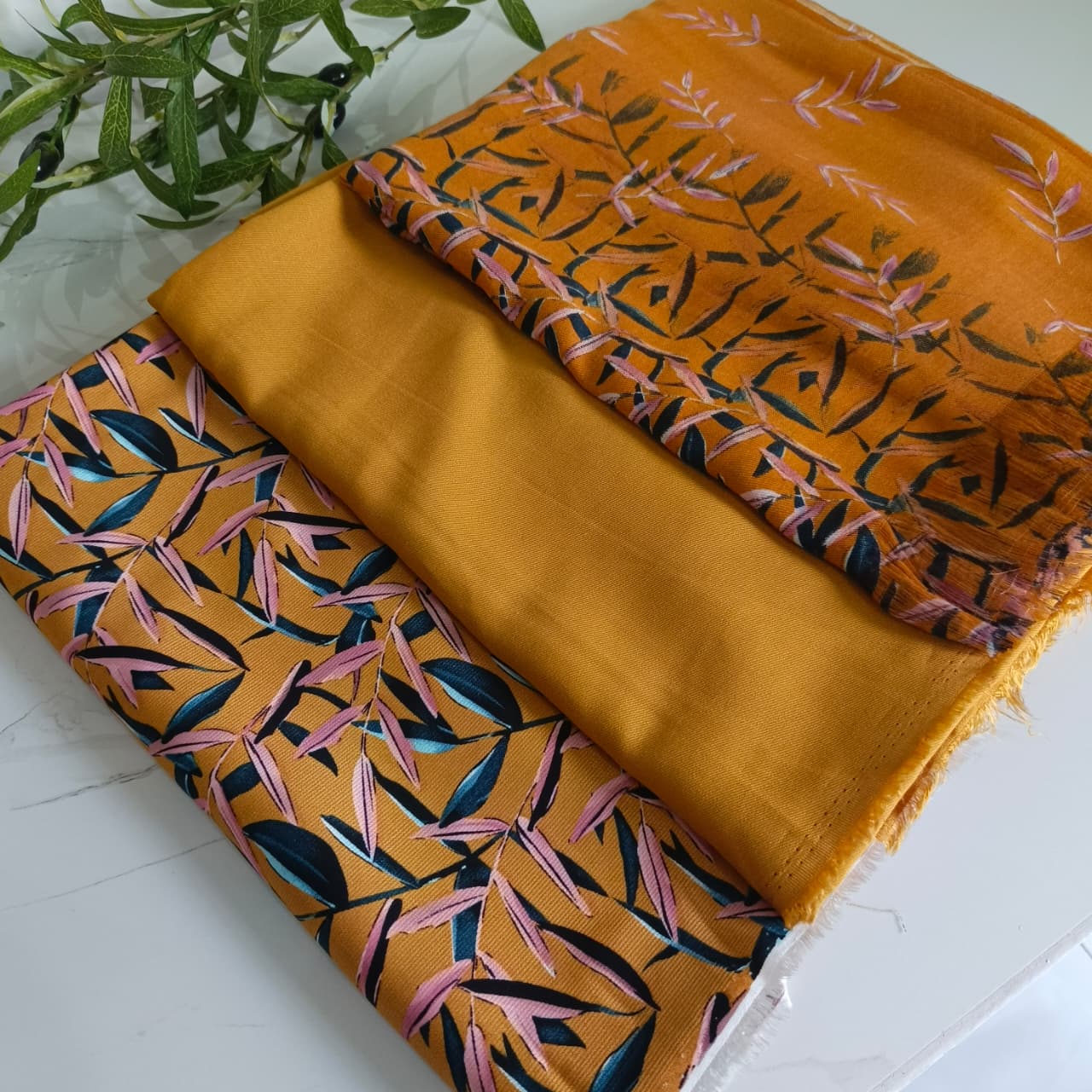 Two pieces of orange fabric with leaf patterns on a white surface.