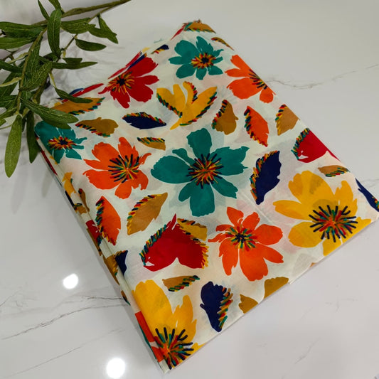 Colorful floral fabric on a off-white surface with a plant leaf.