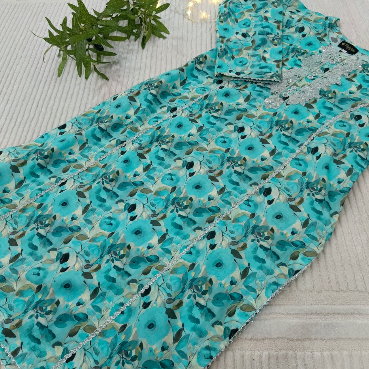 Turquoise floral fabric on a light gray surface with green leaves.
Celebrate Eid with Noor-e-Zar Collection - Flat 25% Off Festive Pakistani Dresses Online