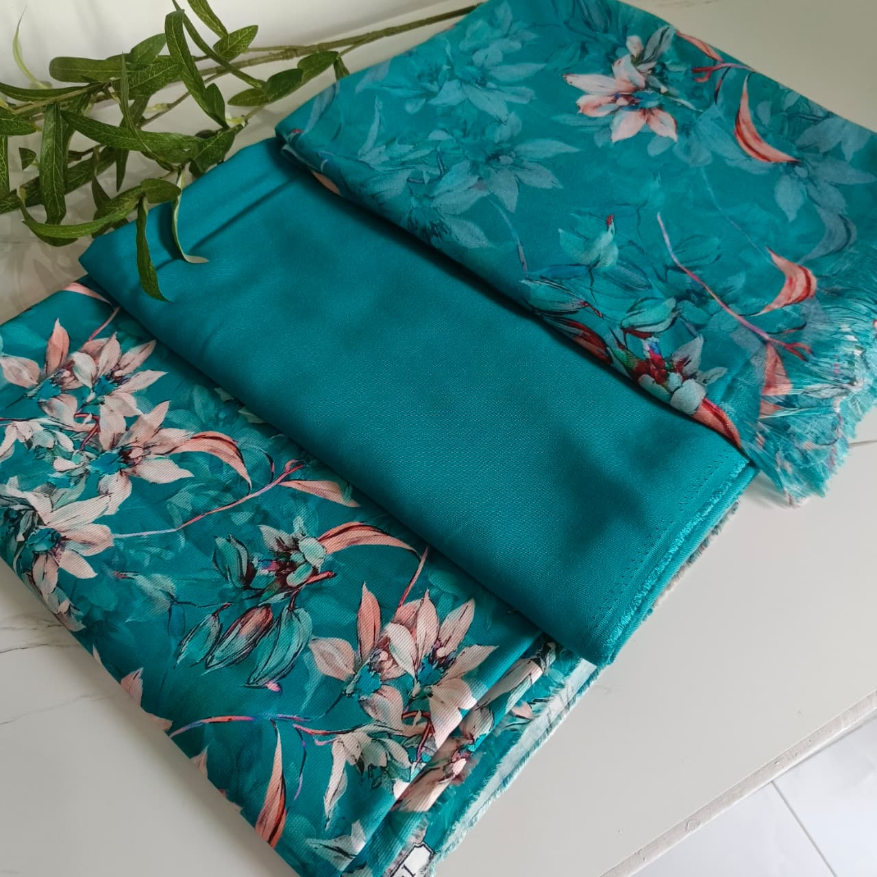 Two turquoise fabric swatches with floral patterns on a white surface.